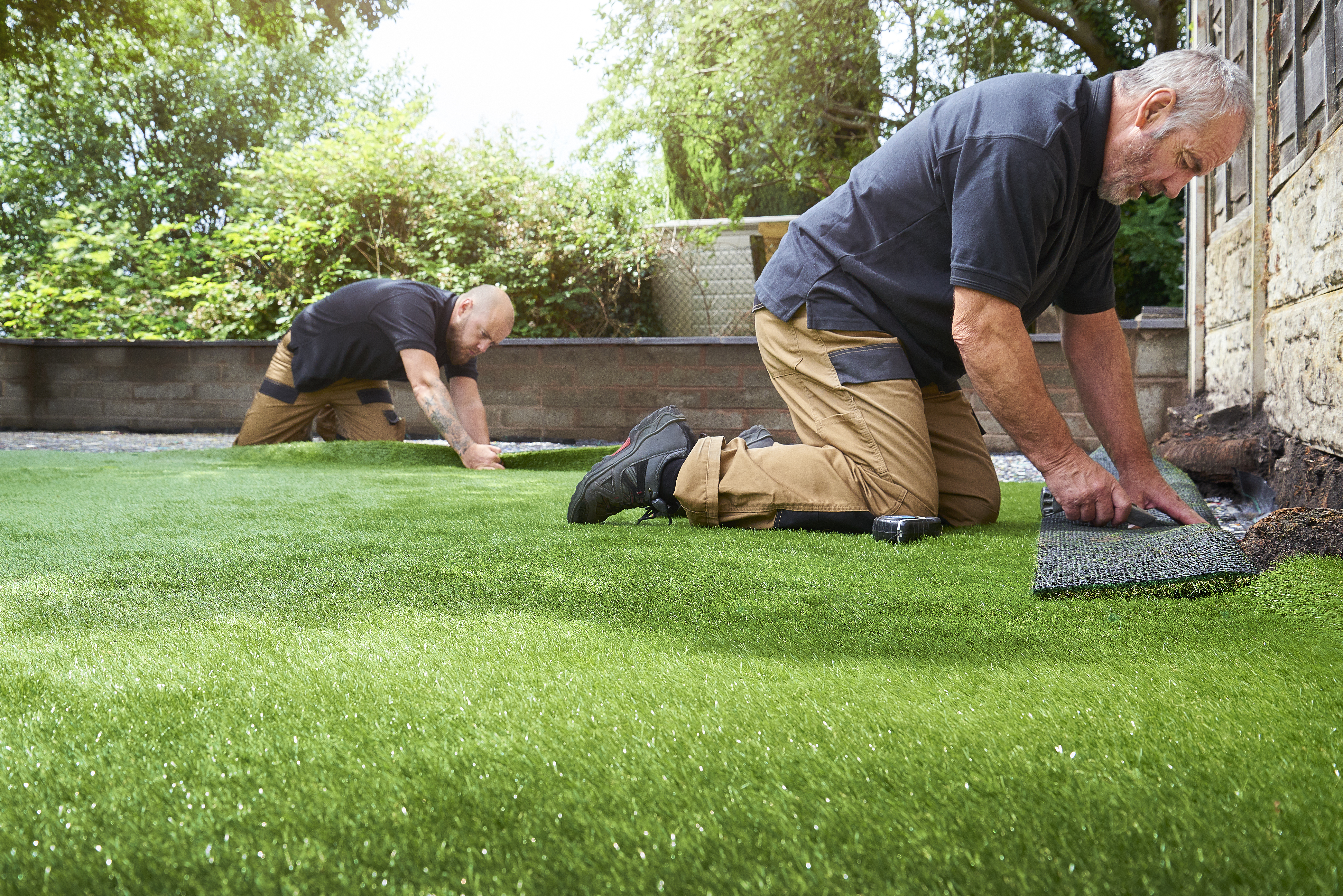 two workers fitting artificial grass in home garden
