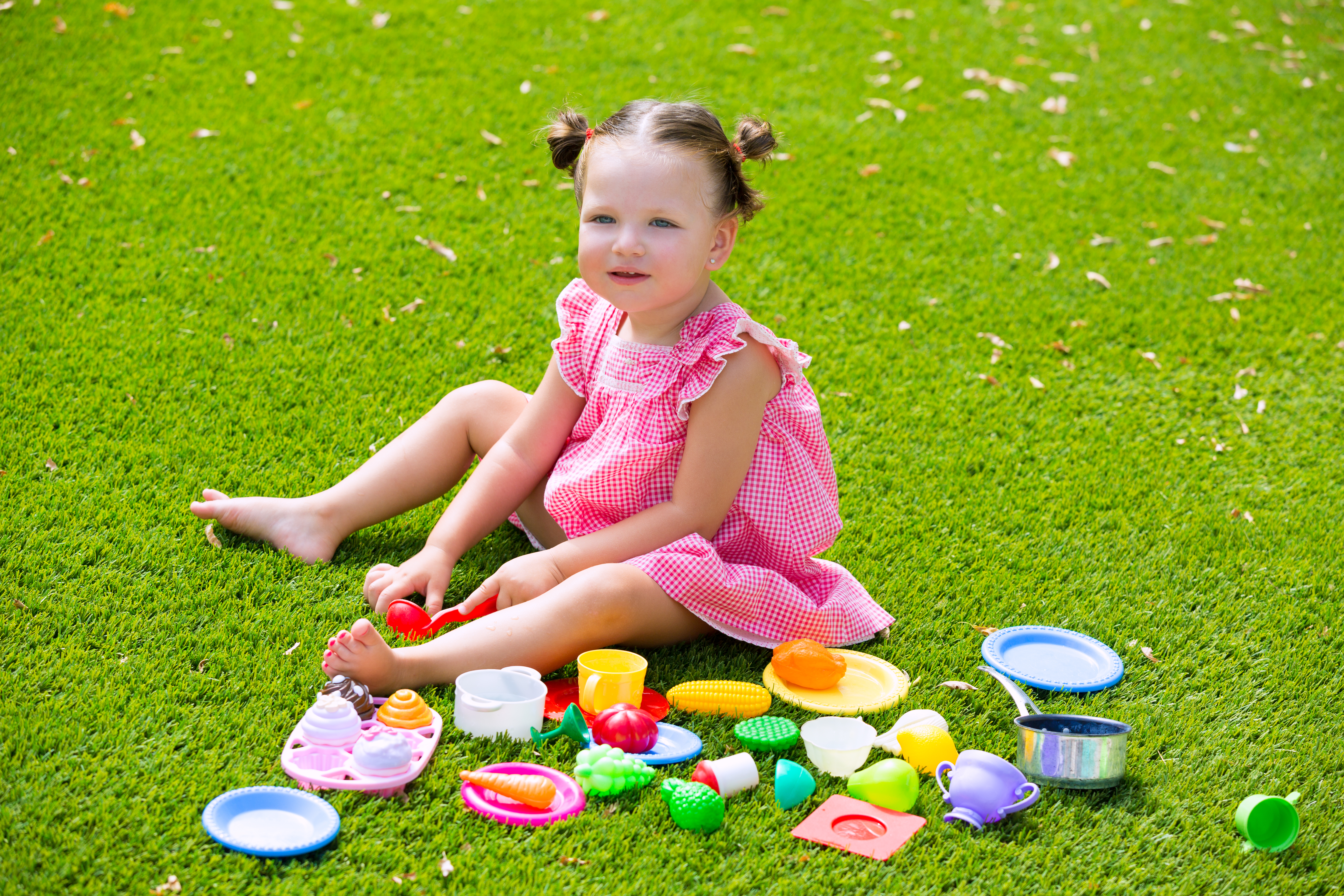 Toddler kid girl playing with food toys sitting in green turf grass garden